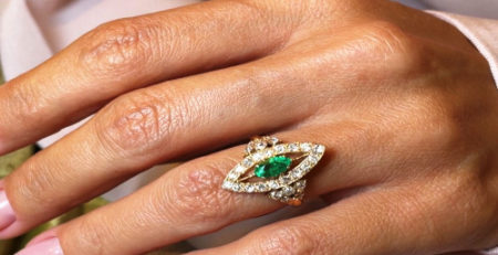 engagement ring with diamonds and emerald worn by a lady on the left hand and